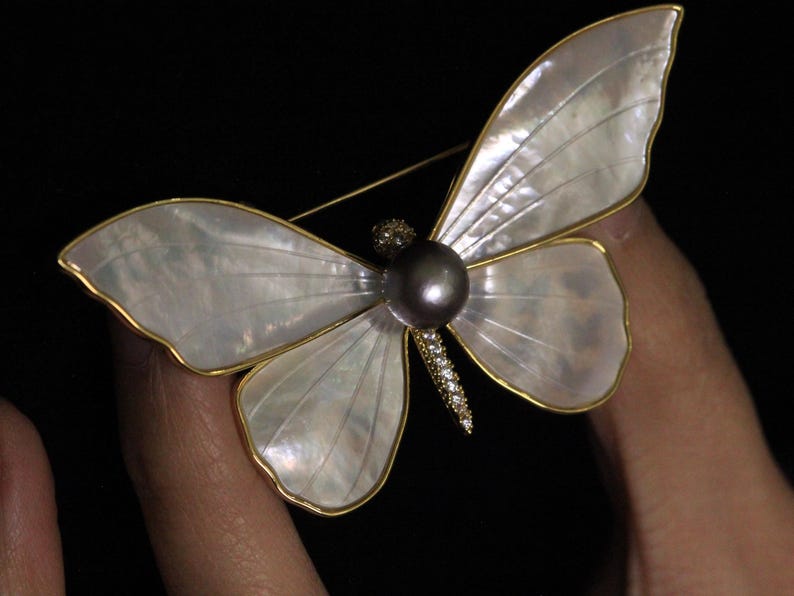 May include: A gold butterfly brooch with a pearl accent. The wings are made of iridescent mother of pearl.