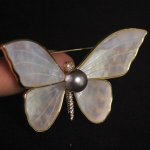 May include: A gold butterfly brooch with iridescent white wings and a black pearl in the centre.