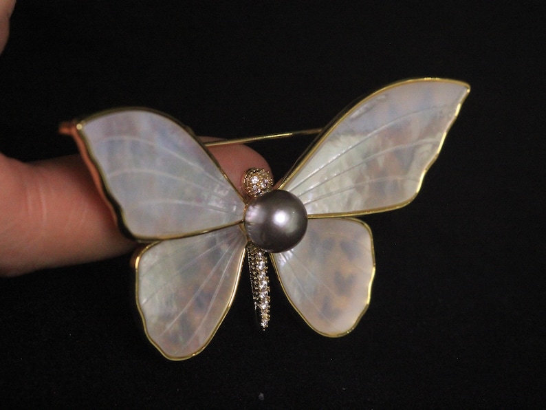 May include: A gold butterfly brooch with iridescent white wings and a black pearl in the centre.