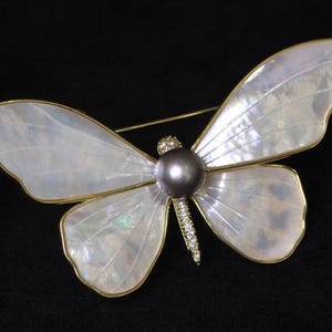 May include: A gold butterfly brooch with iridescent white wings and a dark grey pearl in the centre. The wings are detailed with a delicate gold trim.