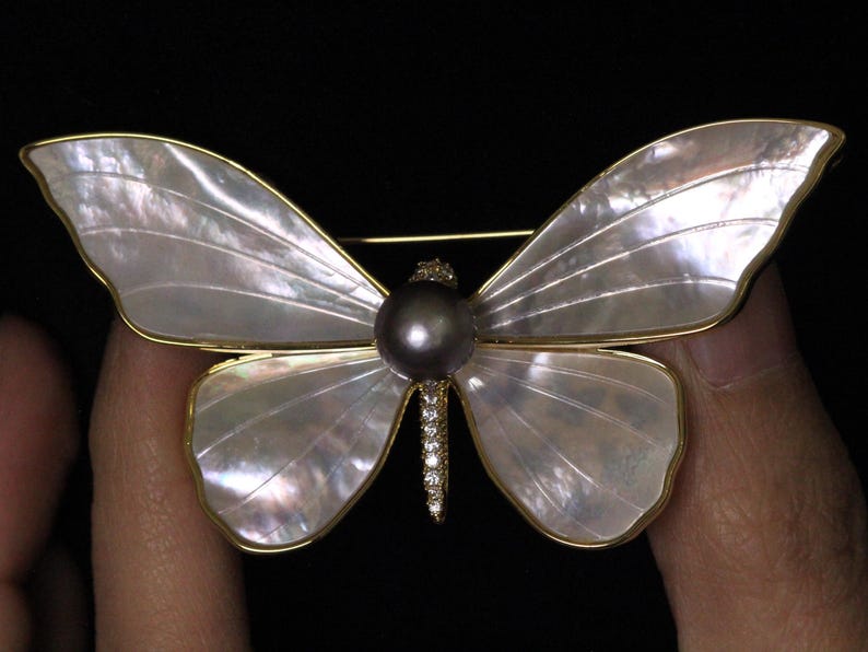 May include: A gold butterfly brooch with a large black pearl in the centre and a row of clear rhinestones on the body.