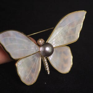 May include: A white mother of pearl butterfly brooch with a dark grey pearl and clear rhinestones.