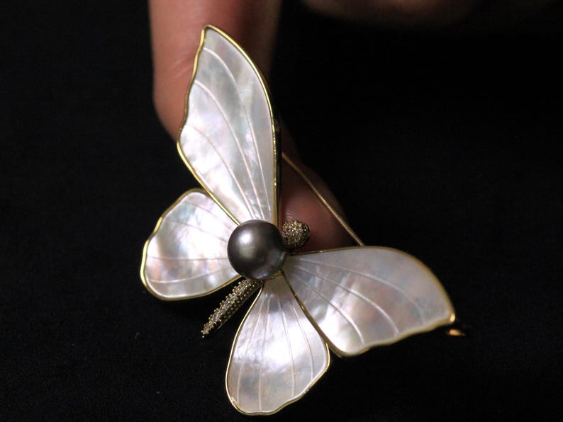 May include: A gold butterfly brooch with white mother of pearl wings and a black pearl in the centre.