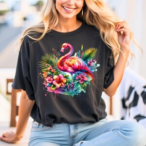 May include: A black t-shirt with a colorful flamingo and tropical flowers graphic print. The flamingo is pink, orange, and yellow, and the flowers are pink, yellow, and blue. The graphic is surrounded by green leaves.