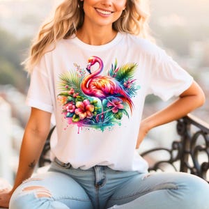 May include: White t-shirt with a colorful flamingo and tropical flowers graphic print. The flamingo is pink, orange, and yellow with a long neck and long legs. The flowers are pink, yellow, and orange. The background is a watercolor wash of pink, blue, and green.