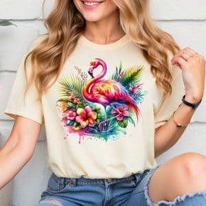 May include: A light yellow t-shirt with a colorful flamingo standing in a pool of water surrounded by tropical flowers and leaves.