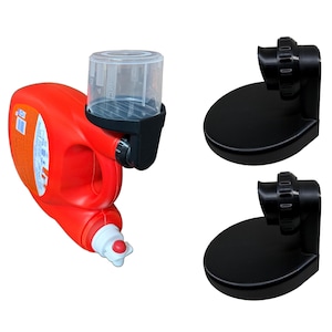 May include: A red detergent bottle with a clear plastic measuring cup attached, and two black plastic holders. The bottle has a white and blue label. The measuring cup is attached to a black plastic bracket.