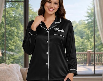 May include: Black satin pajama set with white piping. The long-sleeved top has a notched collar and buttons down the front. The name "Olivia" is embroidered on the chest. The pants are straight-legged.