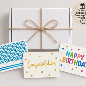 Peut inclure: Une bo&icirc;te cadeau rectangulaire blanche nou&eacute;e avec de la ficelle brune, accompagn&eacute;e de trois cartes de v&oelig;ux. Une carte pr&eacute;sente un motif g&eacute;om&eacute;trique bleu, une autre des pois dor&eacute;s avec le texte Congratulations et la troisi&egrave;me HAPPY BIRTHDAY.