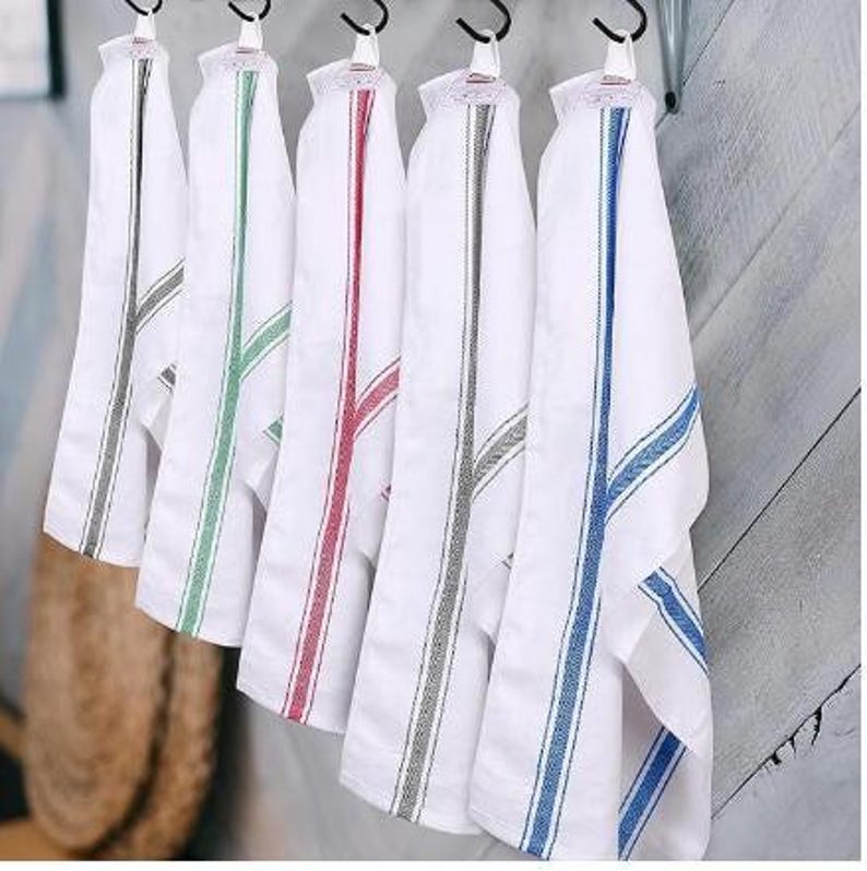 Five white cotton bread tea towels hanging on hooks, each with a different colored stripe: gray, green, red, black and blue.