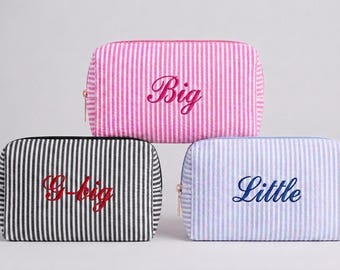Peut inclure: Trois trousses rectangulaires zippées à rayures. La trousse du haut est rose et blanche avec le mot Big brodé en rose. La trousse en bas à gauche est noire et blanche avec G-big en rouge. Celle en bas à droite est bleue et blanche avec Little en bleu.