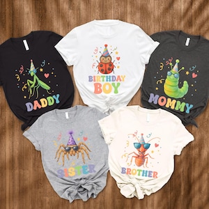 May include: Five short-sleeved t-shirts with insect and family-themed graphics. The shirts are black, white, gray, and off-white. Each shirt features a different insect wearing sunglasses and a party hat, with the words "Daddy", "Birthday Boy", "Mommy", "Sister", and "Brother".