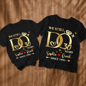 May include: Two black t-shirts with gold text and graphics. The text reads "We Still Do 30 Years Sophia frank -Since 1995- ". The graphic is a stylized gold ring with a diamond.