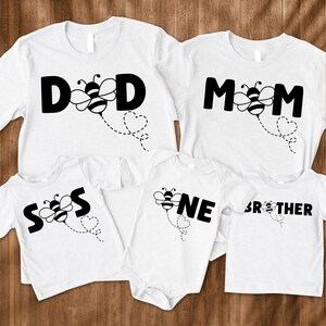 May include: Set of five white t-shirts with black bee and text designs. The shirts say "DAD", "MOM", "SON", "ONE", and "BROTHER".