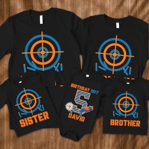 May include: A set of four black t-shirts with a target and darts design. The shirts say "Birthday Boy", "Sister", "Brother", and "David 5".