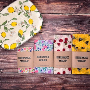 May include: Four different patterned beeswax food wraps with brown paper labels that say "Beeswax Wrap" and the website address. The wraps are on a wooden surface.