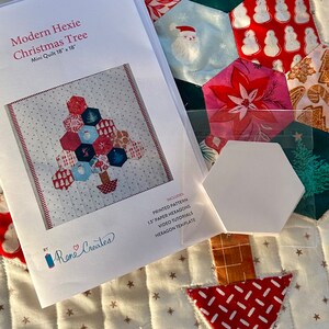 May include: A printed pattern for a modern hexie Christmas tree quilt. The pattern includes 1.5 inch paper hexagons, video tutorials, and a hexagon template. The quilt is 18 inches by 18 inches.