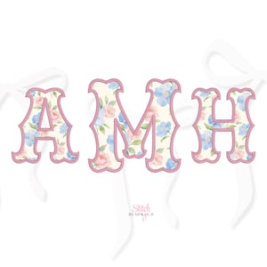May include: Floral embroidered letters spelling "AMH" with a light pink border and white ribbons. The letters are filled with a pattern of blue and pink flowers on a cream background. The "Stitch Ready Hub" logo is visible.
