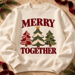 以下が含まれることがあります： クリーム色のクルーネックのスウェットシャツで、ダークレッドの文字で「MERRY TOGETHER」とプリントされています。中央には3本のクリスマスツリーが描かれており、左は赤のチェック柄、中央は緑と白、右は緑のチェック柄のデザインです。