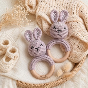 Può includere: Due sonagli a forma di coniglietto all'uncinetto color lavanda con anelli di legno e un paio di scarpine per neonati all'uncinetto. Un anello del sonaglio ha il nome "Emely".