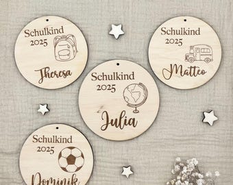Pode incluir: Quatro ornamentos circulares de madeira com o texto "Schulkind 2025" e um nome. Cada ornamento tem um gráfico diferente: uma mochila, um autocarro escolar, uma bola de futebol e um globo. Pequenas decorações em forma de estrela estão espalhadas.