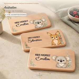 Könnte beinhalten: Drei rechteckige Frühstücksbrettchen aus hellem Holz mit den Maßen 22 x 14 cm. Jedes Brettchen zeigt eine gedruckte Illustration eines Koalas oder Kängurus, florale Akzente und den Text "Hier krümelt" gefolgt von einem Wunschnamen.