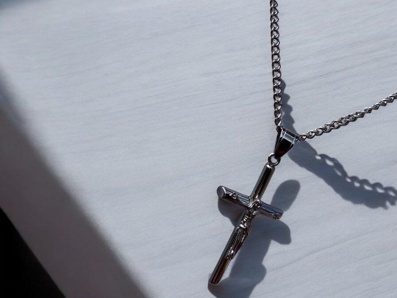 May include: A silver chain necklace with a silver cross pendant featuring a figure of Jesus Christ.