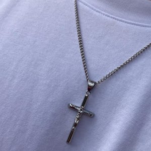 May include: A silver chain necklace with a silver crucifix pendant.