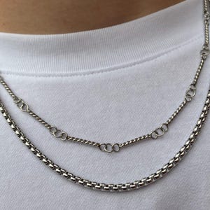 May include: Two silver chains, one a box chain and the other a twisted chain, layered on top of each other.
