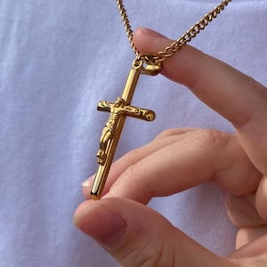 May include: A gold chain necklace with a gold crucifix pendant featuring a detailed figure of Jesus Christ.