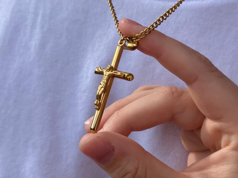 May include: A gold chain necklace with a gold crucifix pendant featuring a detailed figure of Jesus Christ.