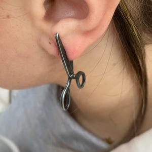 May include: A pair of black scissor earrings. The earrings are made of metal and have a realistic scissor design.