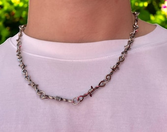 Könnte beinhalten: Eine silberne Kettenkette mit Stacheldrahtgliedern. Die Kette ist verdreht und hat einen silbernen Verschluss.