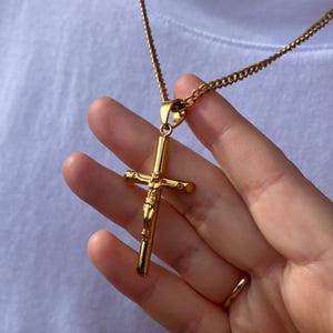 May include: A gold chain necklace with a large gold cross pendant featuring a figure of Jesus Christ.