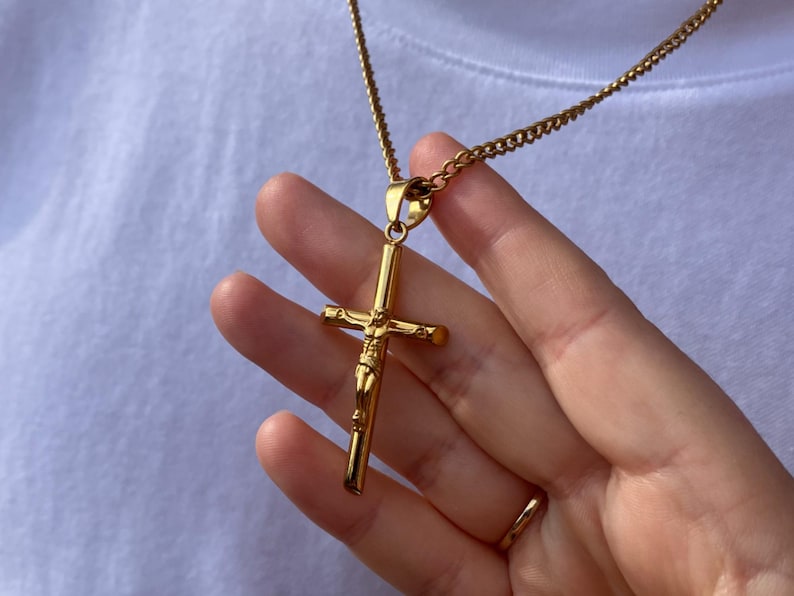May include: A gold chain necklace with a large gold cross pendant featuring a figure of Jesus Christ.