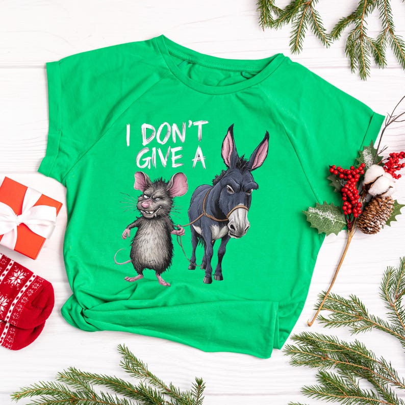 Peut inclure: Un t-shirt vert vif avec l'inscription blanche "I DON'T GIVE A". Le t-shirt pr&eacute;sente une illustration de dessin anim&eacute; d'une souris grise tenant une corde attach&eacute;e &agrave; un &acirc;ne bleu fonc&eacute;. L'&acirc;ne a une corde autour du cou.