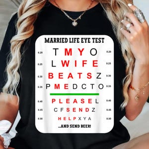 Może przedstawiać: Czarny t-shirt z zabawną grafiką "Married Life Eye Test". Grafika przypomina tablicę okulistyczną, z frazami takimi jak "WIFE BEATS Z" i "...AND SEND BEER!" wydrukowanymi w różnych rozmiarach i kolorach.