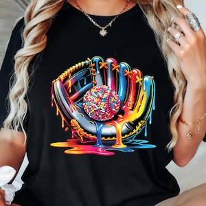 Op de afbeelding: Zwart T-shirt met een kleurrijke afbeelding van een honkbalhandschoen die een honkbal vasthoudt. De handschoen is zwart met blauwe, rode en gele accenten, en de honkbal is bedekt met kleurrijke hagelslag.