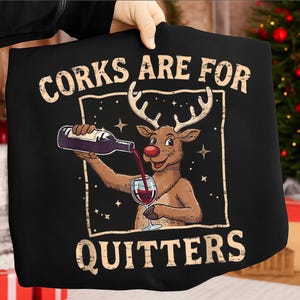 May include: Black t-shirt featuring a cartoon reindeer pouring wine into a glass. The text "Corks Are For Quitters" is displayed above and below the reindeer illustration. The design has a vintage, slightly distressed look.