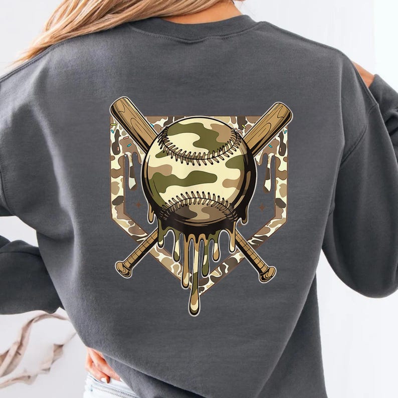 May include: A grey sweatshirt with a baseball-themed design. The design features a camouflage baseball with dripping details, crossed baseball bats, and a diamond-shaped background. The sweatshirt is a comfortable, casual style.