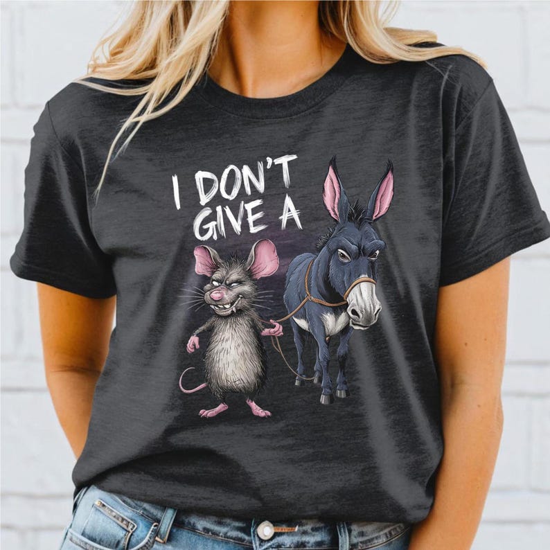Peut inclure: T-shirt gris fonc&eacute; avec une illustration de dessin anim&eacute; d'une souris menant un &acirc;ne. La souris a une expression narquoise et l'&acirc;ne semble indiff&eacute;rent. Le texte "I DON'T GIVE A" est au-dessus de l'illustration.