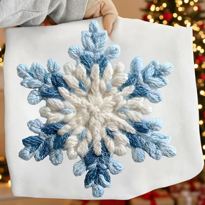 May include: A large, handmade snowflake decoration. The snowflake is crafted from yarn in shades of white, light blue, and dark blue. The snowflake is held against a white background, with a Christmas tree and lights visible in the background.