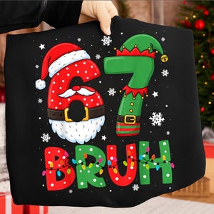 Puede incluir: Camiseta negra con los números 6 y 7 diseñados como Papá Noel y un elfo, respectivamente. La palabra "BRUH" está debajo de los números, decorada con luces navideñas. Copos de nieve y estrellas blancas salpican el diseño.