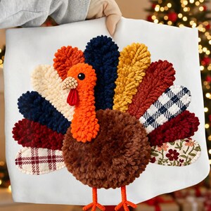 Op de afbeelding: Een wit kussen met een kleurrijk kalkoenontwerp. De kalkoen heeft een bruin lichaam, een oranje kop en een waaier van veren in tinten blauw, geel, rood en stoffen met patronen. De poten van de kalkoen zijn oranje.