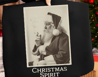 Könnte beinhalten: Schwarze Tragetasche mit einem sepiafarbenen Bild von Santa Claus, der eine Zigarette raucht. Santa trägt seinen traditionellen roten Anzug und Hut mit weißem Besatz. Der Text "CHRISTMAS SPIRIT" ist unten auf dem Bild in Weiß gedruckt.