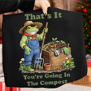 May include: Black t-shirt featuring a cartoon frog in overalls and a straw hat, holding a garden fork. The frog stands next to a compost bin with the text "That's It, You're Going In The Compost".