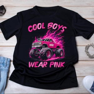 May include: Black t-shirt with a pink graphic of a monster truck engulfed in flames. The text "COOL BOYS" is above the truck, and "WEAR PINK" is below. The truck has the words "CANCER CRUSHER" on the side.