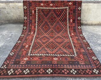 May include: A large rectangular area rug featuring a deep red and dark brown color palette. The central field displays a repeating diamond pattern, framed by a white border and an outer decorative border with geometric motifs in white and blue.