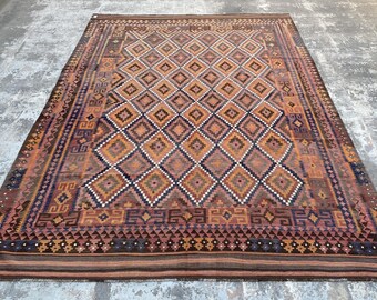 May include: A traditional rug with a diamond pattern in shades of brown, orange, and cream. The rug has a detailed border with geometric designs.