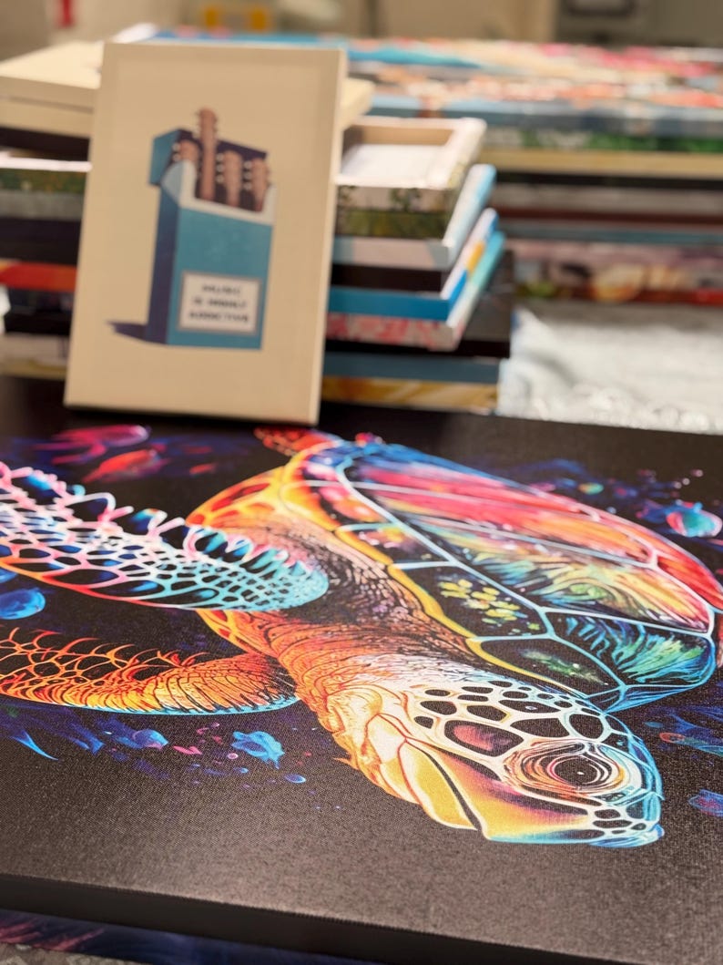 Puede incluir: Una vibrante impresi&oacute;n en lienzo que presenta una colorida tortuga marina con un patr&oacute;n de caparaz&oacute;n detallado. La obra de arte muestra un espectro de tonos, incluyendo naranja, amarillo, azul y rojo, sobre un fondo oscuro. Un libro con un dise&ntilde;o de caja de cigarrillos est&aacute; en el fondo.